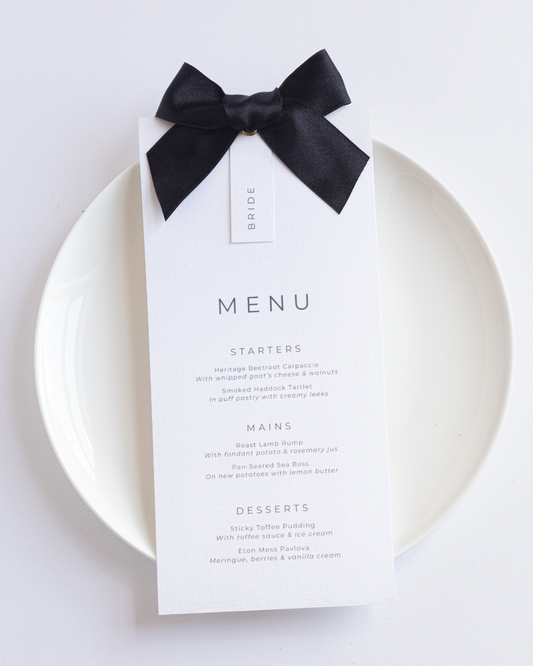 Flat lay of Lilah ribbon wedding menu with satin ribbon and neutral place setting